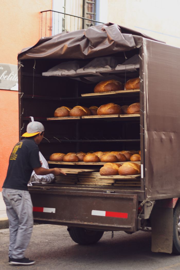 Man loading fresh artisanal bread into a truck on a city street.